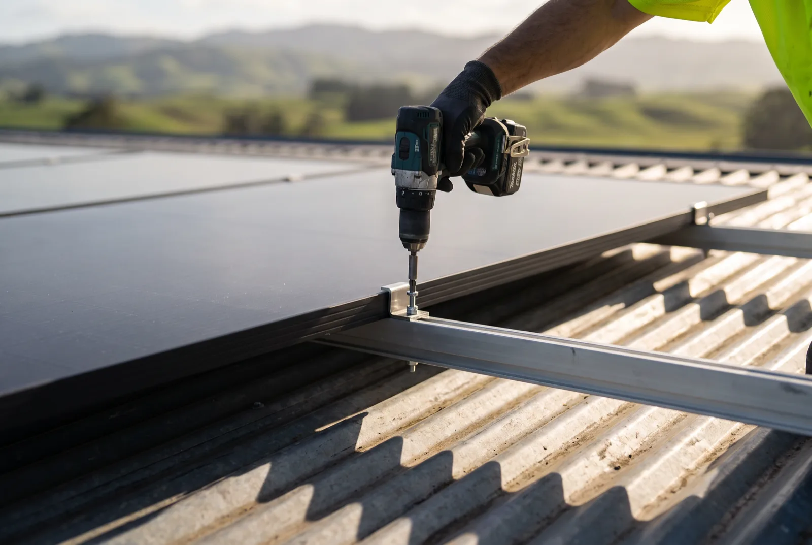 An installer's gloved hands tightening a panel mid-clamp to a mounting rail on a corrugated roof